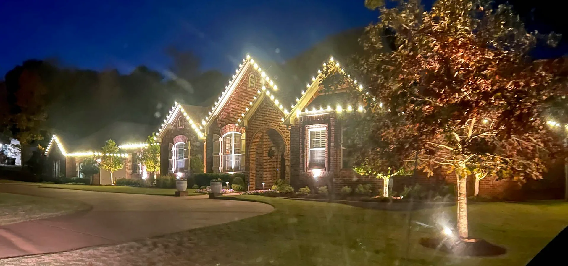 Home with professionally installed warm white Christmas lights along the roofline at dusk